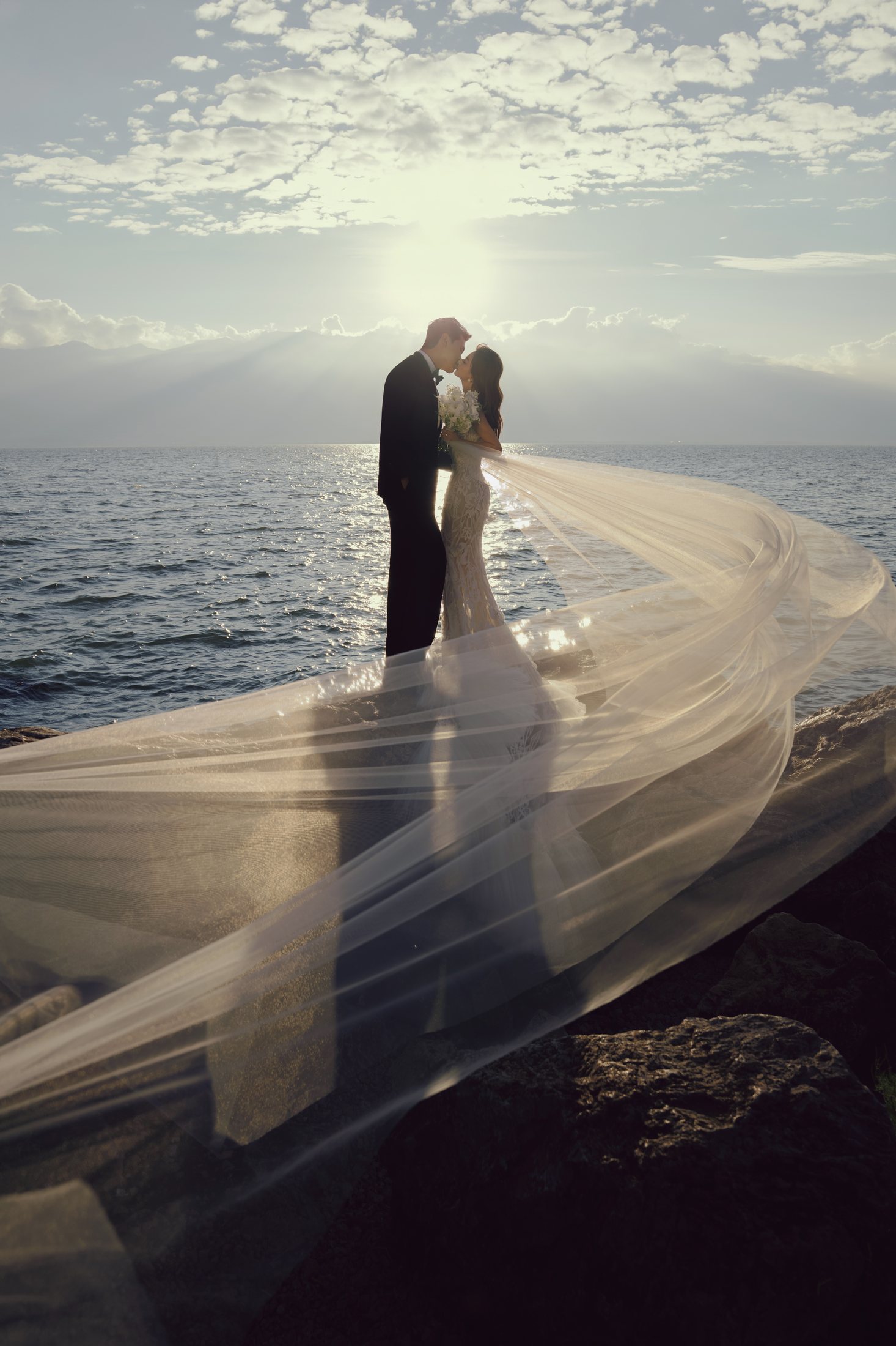 Couple embracing by the water beneath a flowing veil